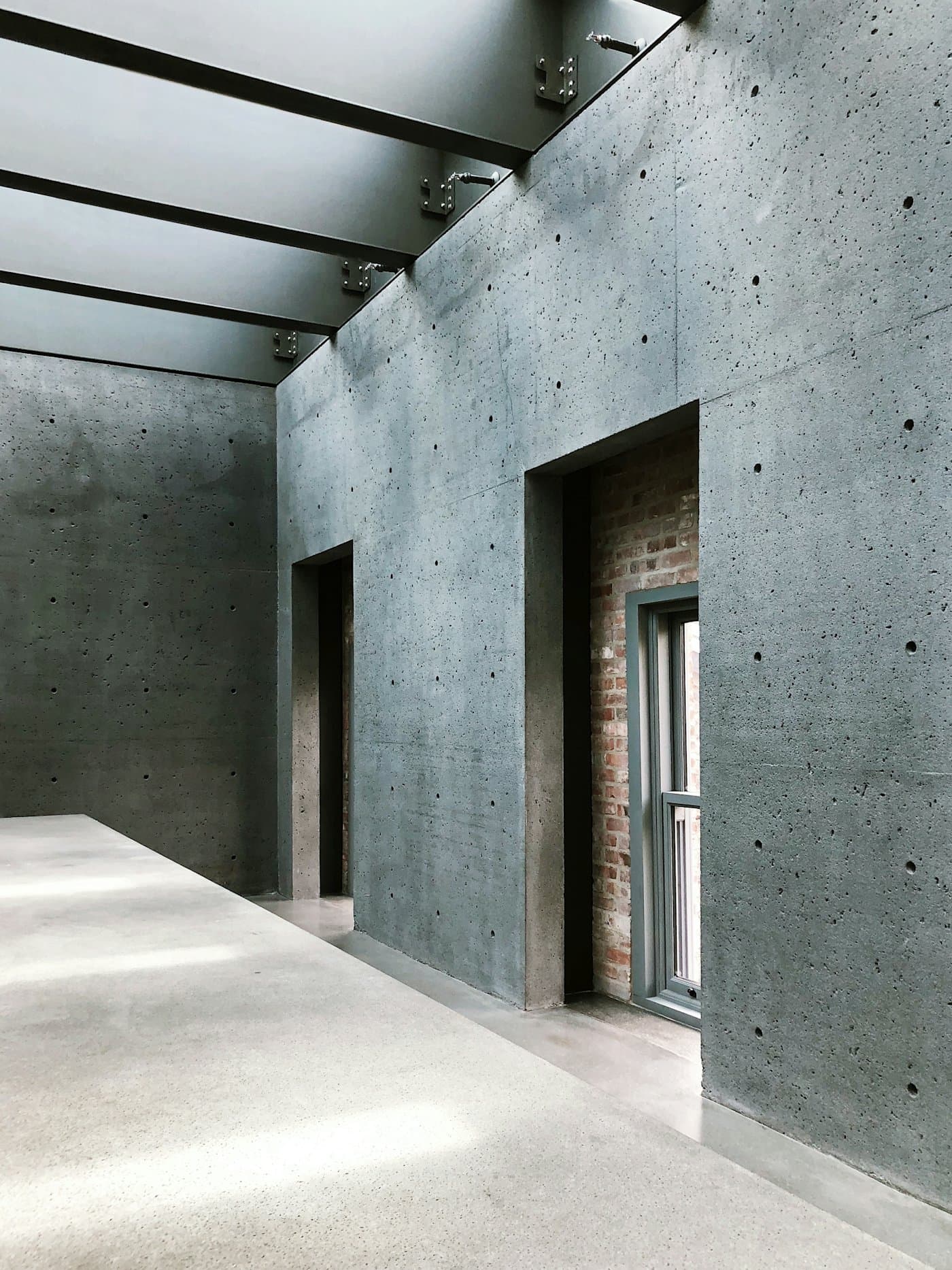 Board-formed concrete walls and a pale terrazzo floor under a glazed skylight, with crisp daylight falling across the floor