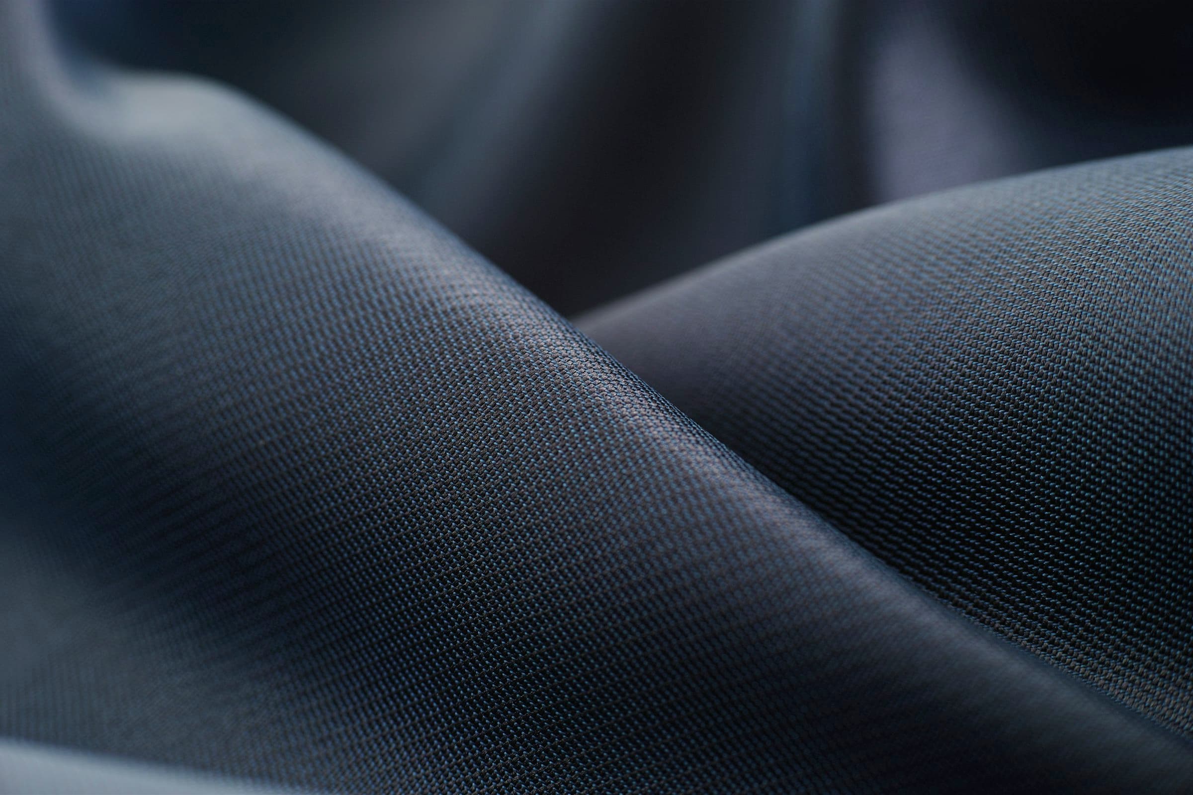 Macro of navy twill fabric falling in smooth sweeping folds under soft directional light