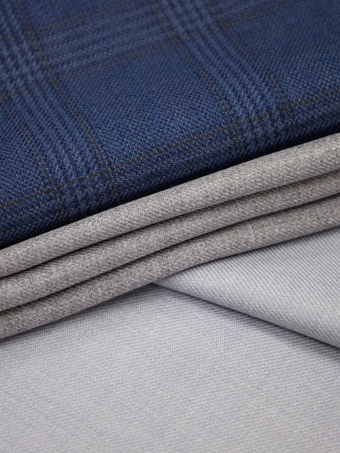 Folded layers of navy check wool, mid-gray flannel and pale gray twill stacked in soft diagonal folds